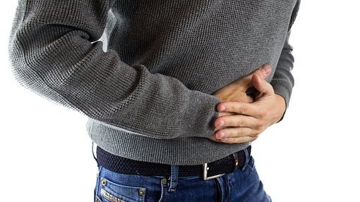 Man in a gray sweater and jeans clutching his stomach in pain